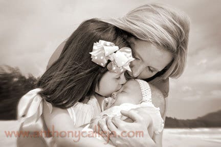 Mother Caresses her children as her 2-year-old daughter holds and kisses her newborn sister