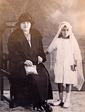 "First Communion portrait of my mother, Theresa Caruana Calleja, taken around 1927. Sitting proudly beside her is her aunt and godmother—her parrina—Lucy Mercieca. This touching photograph captures a sacred milestone in my mother's early life and reflects the close family bonds and strong faith that shaped her upbringing. The presence of her beloved parrina Lucy adds a layer of warmth and tradition to this cherished moment."